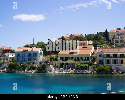 Tradizionali case costiere del villaggio di Fiskardo con il mare calmo di fronte. Un tranquillo e colorato porto dell'isola greca. Foto Stock