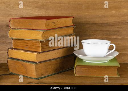 Vista ravvicinata di vecchi libri colorati con tazza di caffè in ceramica bianca su un tavolo di legno Foto Stock