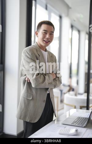 Sorridente giovane uomo d'affari asiatico in un ufficio moderno. bell'uomo asiatico felice e amichevole mentre lavora lavoro di successo Foto Stock
