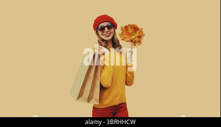 Abito in stile autunnale, ritratto di una bella giovane donna con borsa della spesa contiene foglie d'acero gialle con cappello rosso di berretto francese e maglione in maglia Foto Stock