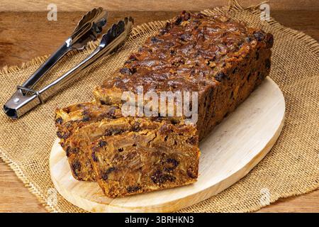 Fetta di deliziosa torta di frutta fatta in casa su una tavola di legno con una pinza metallica su un sacco su un tavolo di legno Foto Stock