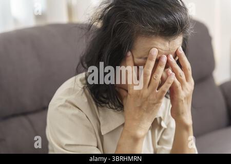 Triste donna asiatica di mezza età che tocca la fronte con mal di testa che soffre di emicrania. donna asiatica matura che si sente male o depressione Foto Stock