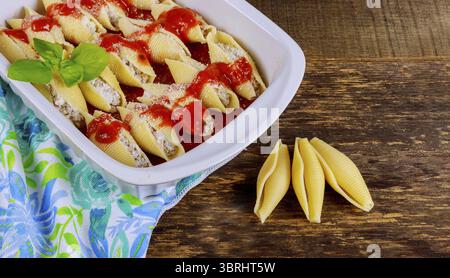 Conchiglie di pasta ripiene di formaggio e funghi, cosparse di parmigiano in piatto da forno Foto Stock