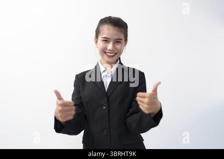 Positivo asiatico giovane donna d'affari che mostra pollice in su guardando la fotocamera su sfondo bianco che controlla per un buon lavoro Foto Stock