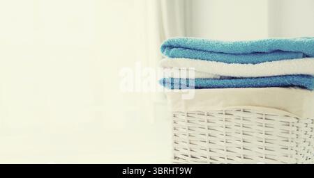 Cestino per bucato in vimini con asciugamani piegati puliti sul letto Foto Stock