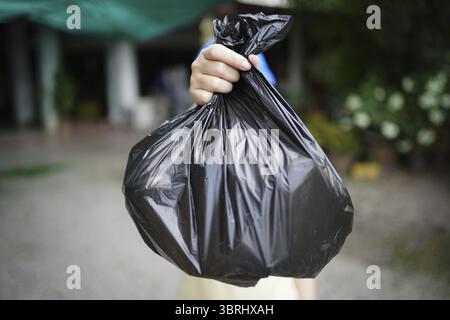 Donatrice volontaria che tiene a mano il sacchetto nero della spazzatura e la spazzatura della bottiglia di plastica per il riciclaggio per la pulizia nel parco volontariato concetto Reuse and vo Foto Stock