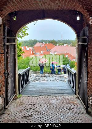 Vista panoramica attraverso le porte ad arco dell'antica fortezza fino ai tetti di tegole rosse e alle persone con ombrelli a Petrovaradin, Serbia Foto Stock