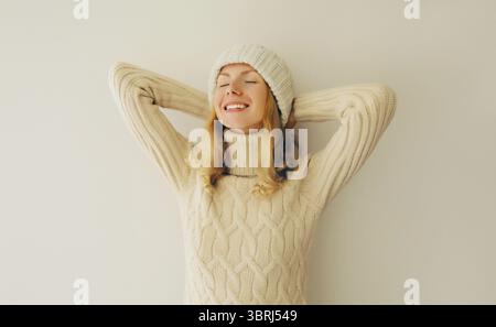 Rilassata e felice donna sorridente a occhi chiusi tiene le mani dietro la testa in inverno abiti caldi a maglia, maglione e cappello Foto Stock
