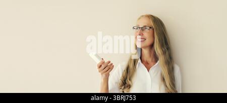 Ritratto di una donna di mezza età caucasica sorridente e felice accende il condizionatore d'aria o la TV utilizzando il telecomando a casa Foto Stock