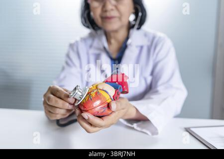 Cardiologa sostiene il medico di cuore anziano donna asiatica che indossa occhiali e uniforme. ritratto di matura vecchia donna asiatica medico professionale Foto Stock