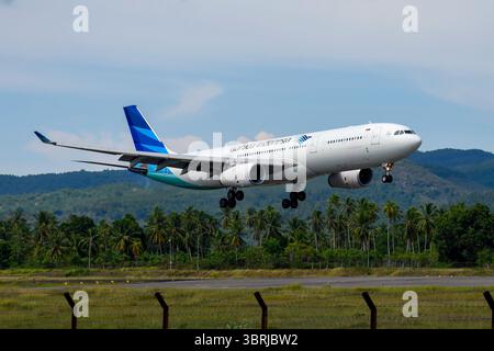 Garuda Indonesia, Airbus A330-300 atterraggio all'aeroporto internazionale Sultan Iskandar Muda Aceh con palme da cocco e vista sulle montagne sullo sfondo dell'aeroporto Foto Stock