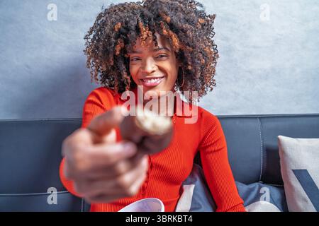 Giovane donna felice che condivide un biscotto ricoperto di cioccolato mentre siede sul divano Foto Stock