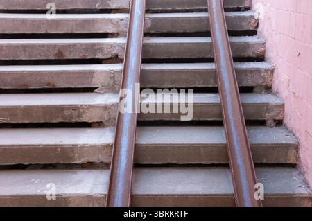 Vecchie scale in cemento in un sottopassaggio, usurate e riparate grossolanamente. Due guide metalliche arrugginite fungono da rampa improvvisata, mostrando segni di decadimento e avvicinamento Foto Stock