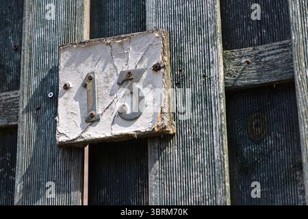 Una casa rustica e intemprata numero '13' su una recinzione di legno angosciata, piena di carattere. Foto Stock