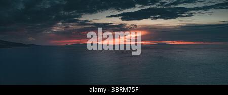 Tramonto mozzafiato che dipinge il cielo con vivaci sfumature su un mare tranquillo, creando un'atmosfera suggestiva e tranquilla Foto Stock
