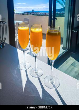 Tre eleganti flute di champagne riempiti di rinfrescanti cocktail mimosa all'arancia sono disposti su un luminoso piano di appoggio, creando un'allegra e invitante colazione Foto Stock