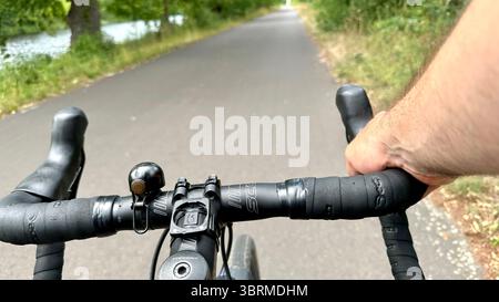 Una strada vista dalla prospettiva di un ciclista su una bicicletta con una mano sul bar Foto Stock