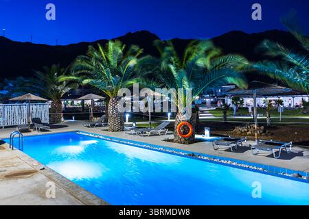 Piscina con palme e lettini illuminati di notte nel giardino tropicale dell'hotel resort. Kardamena. Grecia. Foto Stock