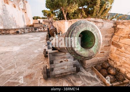 Antico cannone in bronzo su una carrozza in legno all'interno delle mura di un castello medievale affacciato sul mare, con ancora arrugginite e palle di cannone Foto Stock