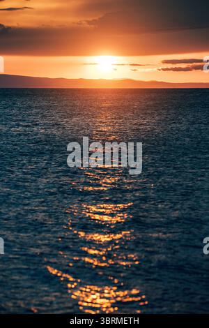 Il sole tramonta sulle calme acque oceaniche, emettendo una calda luce dorata e creando un'atmosfera serena Foto Stock