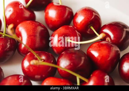 Primo piano di ciliegie rosse fresche. Frutta succosa con gambi verdi. Snack dolce estivo o ingrediente da dessert. Cibo biologico sano. Immagine macro di chery. Foto Stock