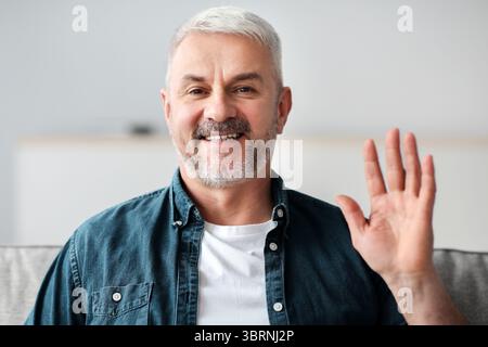 Bell'uomo anziano che ha una videoconferenza, sventolando alla telecamera Foto Stock
