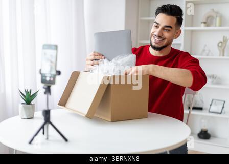 Bel Parcel Blogger maschio arabo Unboxing con laptop sulla macchina fotografica Foto Stock