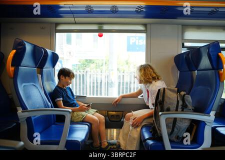 Due bambini si impegnano in una conversazione vivace durante un viaggio in treno, condividendo un momento di connessione mentre sono seduti l'uno di fronte all'altro. La ripresa della scena Foto Stock