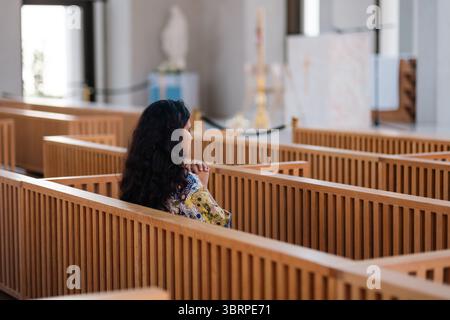 Moderno interno della chiesa cattolica con donna che prega, panchina in legno all'interno della chiesa Foto Stock