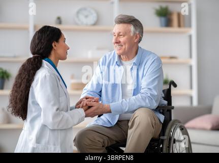 Concetto di assistenza sanitaria per le persone anziane. Medico che tiene le mani di un anziano disabile in sedia a rotelle durante la visita medica Foto Stock