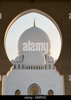 Arco islamico nella grande Moschea di Abu Dhabi, luce dorata su cupola di marmo bianco con luna islamica a mezzaluna - vista orizzontale Foto Stock
