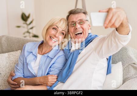 Nonni moderni tenendo selfie sul cellulare, appoggiata sul divano Foto Stock