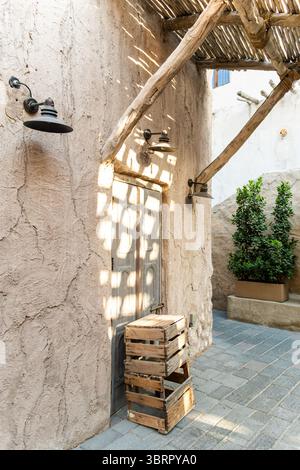 vecchia casa in pietra nel villaggio con tettoia del tetto in bambù, motivi di luce e ombra sulle pareti, pareti in gesso di calce con crepe, vecchia lanterna d'epoca appesa Foto Stock