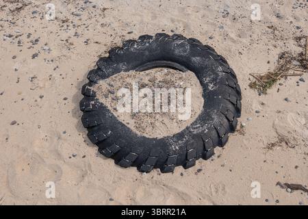 Vecchio pneumatico di gomma per auto sulla spiaggia sabbiosa, parzialmente coperto di sabbia, sfondo astratto. Foto Stock