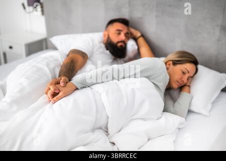 Una giovane coppia sposata sta dormendo nel loro letto. Si tengono per mano e si godono un buon sonno. Foto Stock