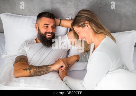 La mattina, una giovane coppia felice e amorevole è sdraiata a letto. Sono rilassanti e sorridenti. Foto Stock