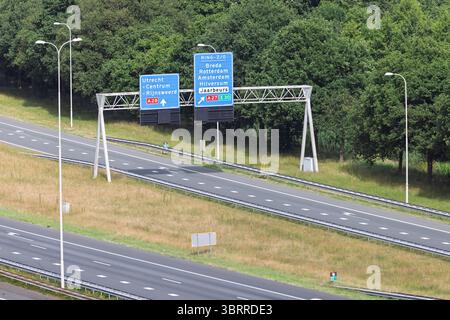 La segnaletica autostradale olandese vicino a Utrecht dirige il traffico verso le principali città e il centro fieristico Jaarbeurs, sullo sfondo di alberi verdi Foto Stock