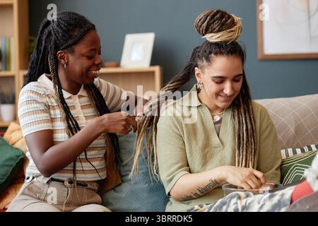Giovane donna nera capelli intrecciati di giovane donna caucasica seduta al chiuso Foto Stock