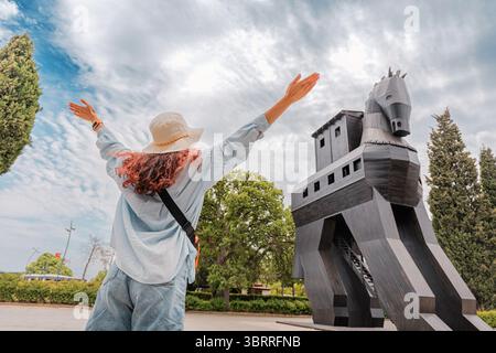 5 maggio 2025, Canakkale, Turkiye: Turista che solleva le armi di fronte alla replica del cavallo di Troia che celebra i viaggi e la storia a Canakkale, Turchia Foto Stock