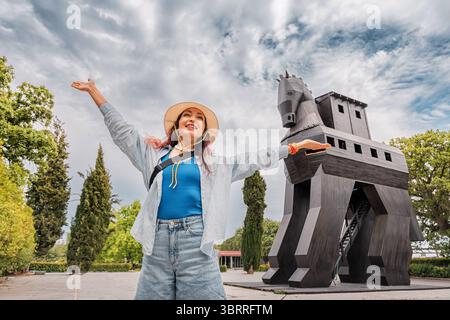 5 maggio 2025, Canakkale, Turkiye: Turista che solleva le armi di fronte alla replica del cavallo di Troia che celebra i viaggi e la storia in Turchia Foto Stock