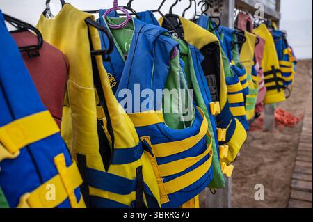 Fila di giubbotti di salvataggio, in spiaggia, pronti per l'affitto Foto Stock