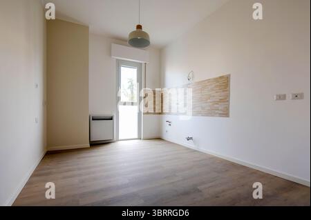 Moderna cucina vuota con pavimento in legno e piastrelle a spruzzo durante i lavori di ristrutturazione, con luce naturale che entra dalla finestra Foto Stock