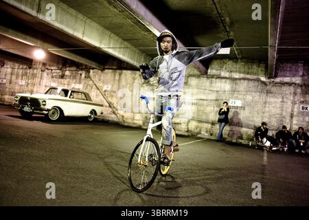 Un gruppo di spettatori guarda un uomo eseguire un trucco su biciclette fisse in un parcheggio a Seattle, Washington. Foto Stock