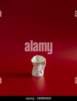 Tazza in carta bianca arricciata su sfondo rosso scuro concetto minimalista Foto Stock