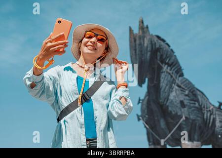 6 maggio 2025, Canakkale, Turchia: Turista femminile che scatta selfie con lo smartphone di fronte al cavallo di Troia Foto Stock