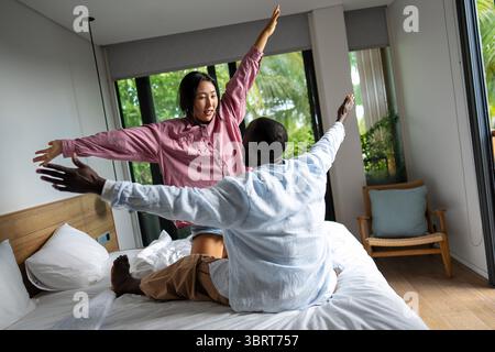 Giovani coppie diverse che sorridono gioiosamente insieme nel loro luminoso soggiorno, indossando abiti casual Foto Stock