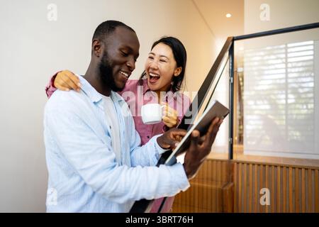 Felice coppia multietnica che utilizza un notebook, acquista online con le vendite, gioca insieme Foto Stock