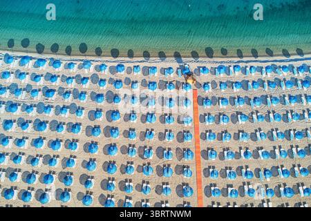 File di ombrelloni e sedie a sdraio che creano un motivo geometrico sulla sabbia accanto all'acqua cristallina turchese Foto Stock