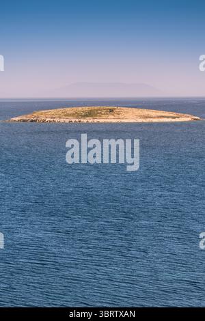 Vista aerea di una piccola isola disabitata circondata da acque blu calme, creando una scena tranquilla e idilliaca Foto Stock