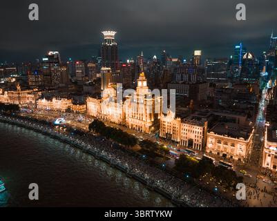 Shanghai, Cina - 21 giugno 2025: Veduta aerea dell'architettura storica del Bund scintillante sotto il cielo notturno, un contrasto luminoso con le acque scure e i lontani grattacieli. Foto Stock
